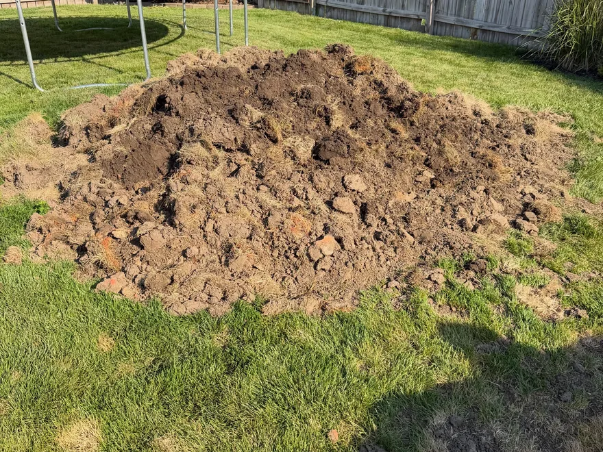 A large pile of dug-up dirt and sod on a backyard lawn