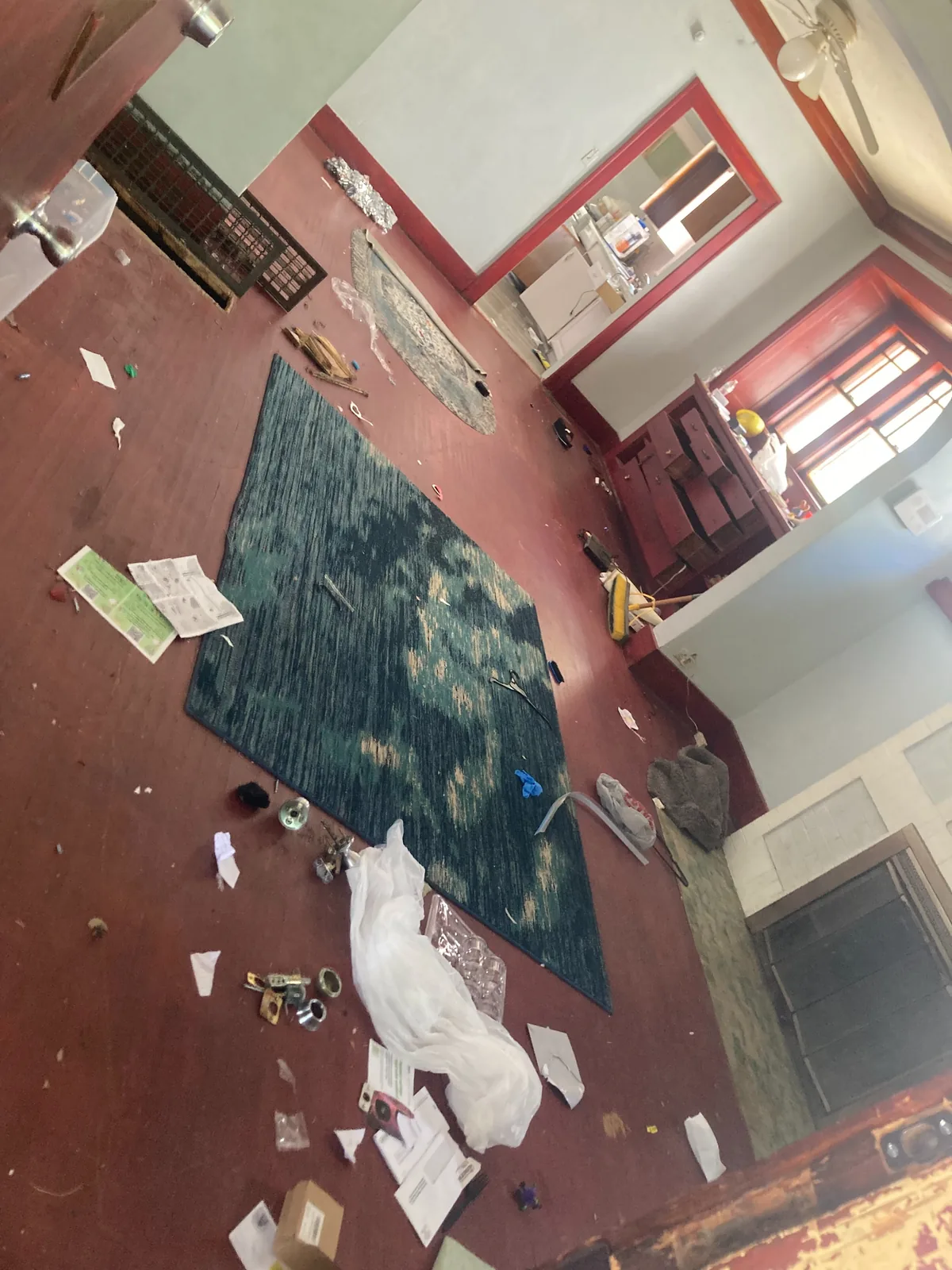 Red hardwood living room in Peoria IL strewn with an old area rug, paper and abandoned belongings before cleanout