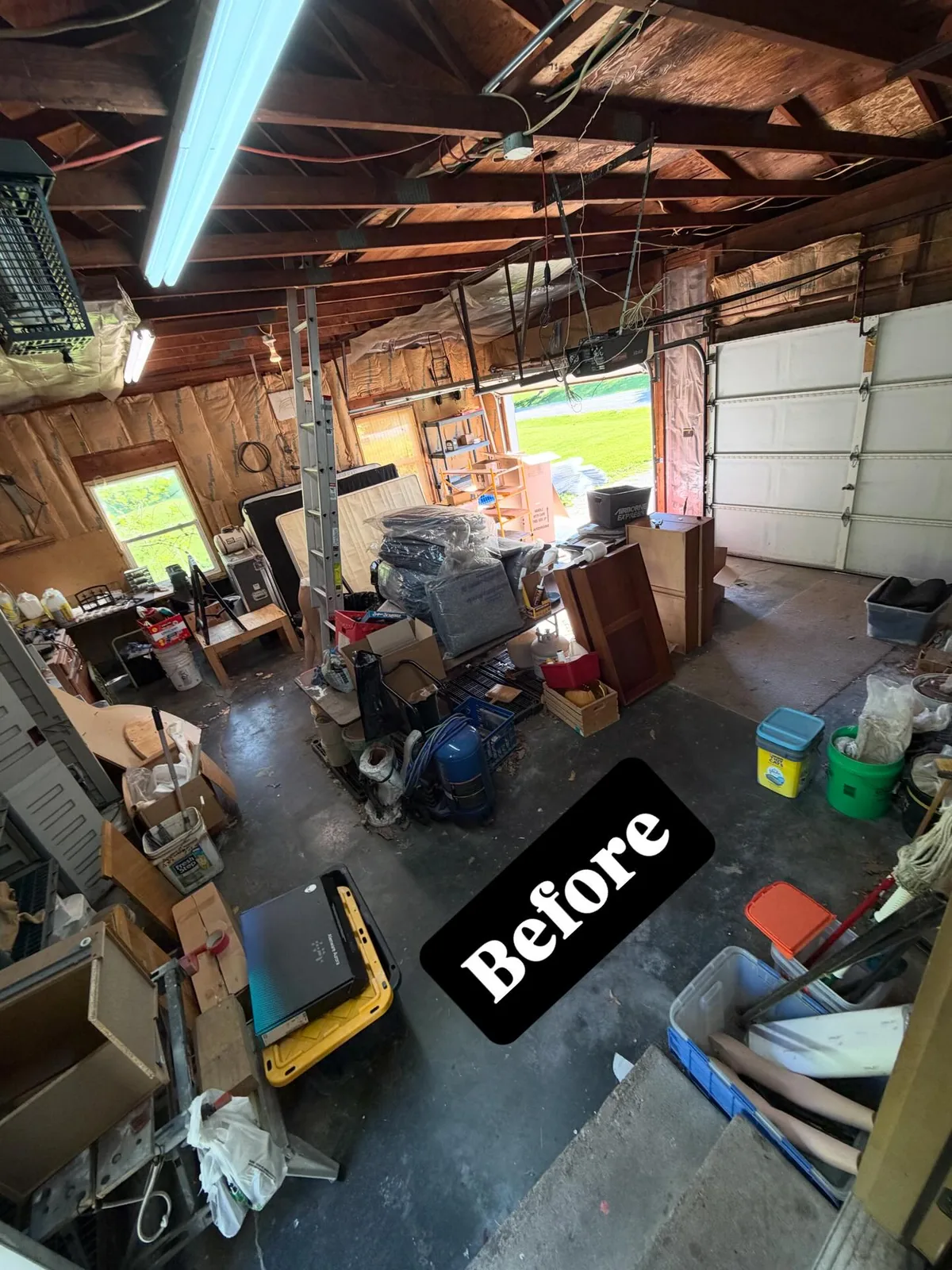 Attached garage in Peoria IL packed with dressers, cabinets, a mattress, shelving and storage totes before a whole house cleanout
