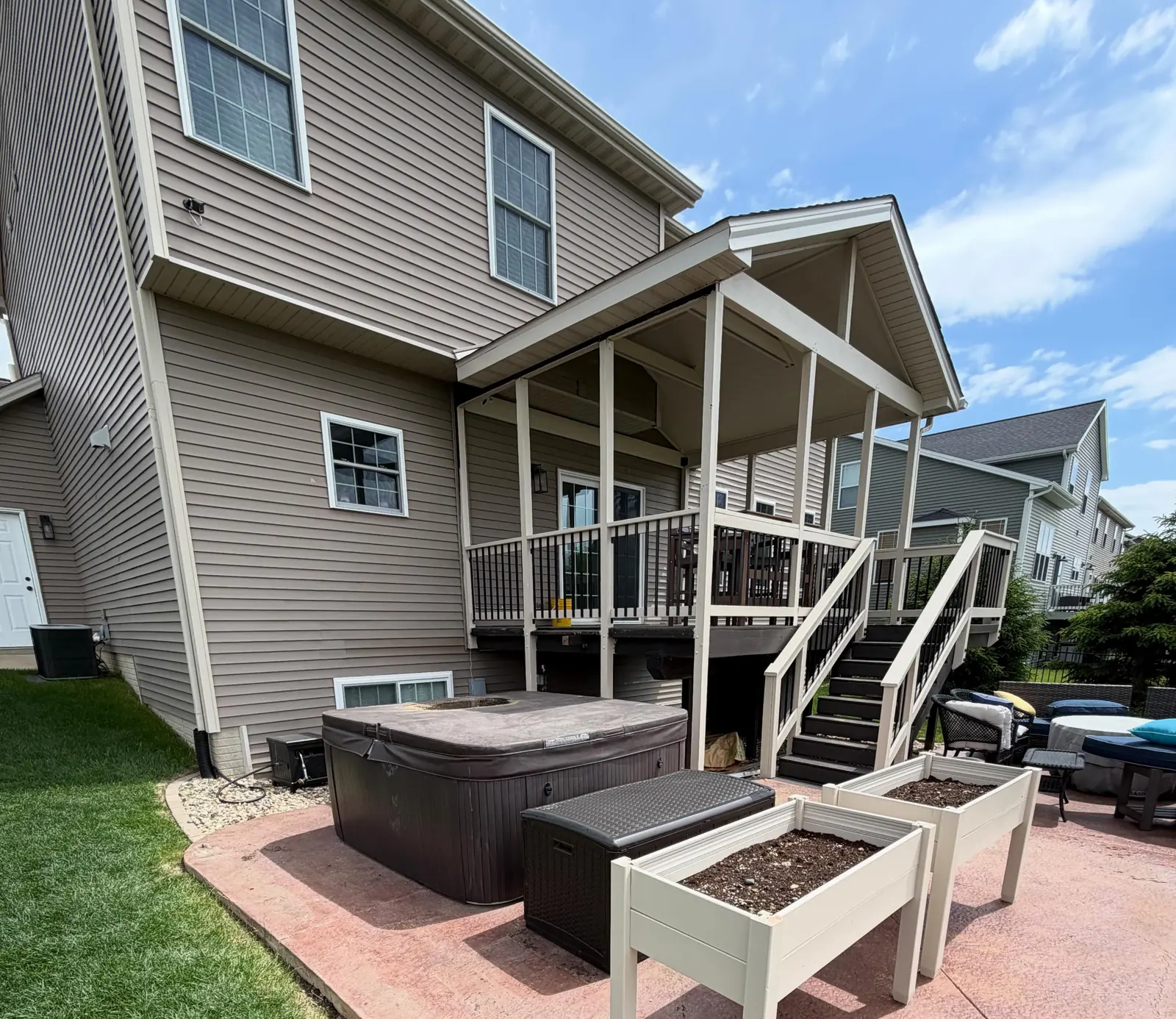 The same stamped concrete patio and hot tub with the pergola gone, open to the sky and the deck stairs clear