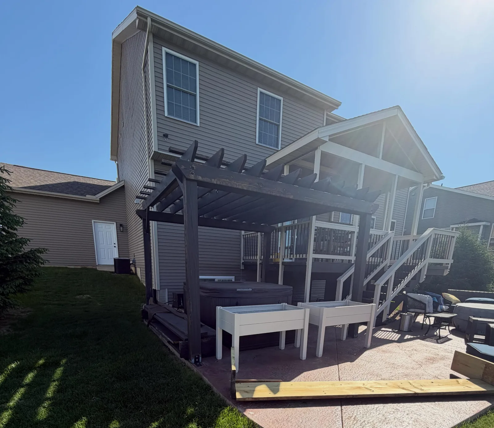 Dark stained wood pergola built over a stamped concrete patio and hot tub behind a two-story home, before teardown