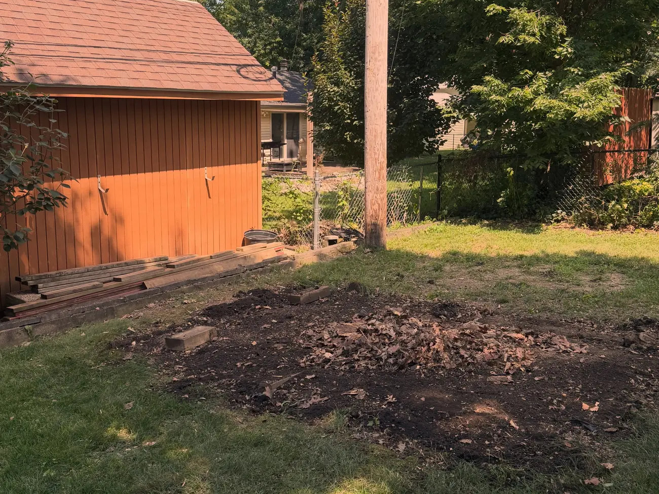 The same back yard with the shed gone, leaving a bare dirt pad beside the red garage and utility pole