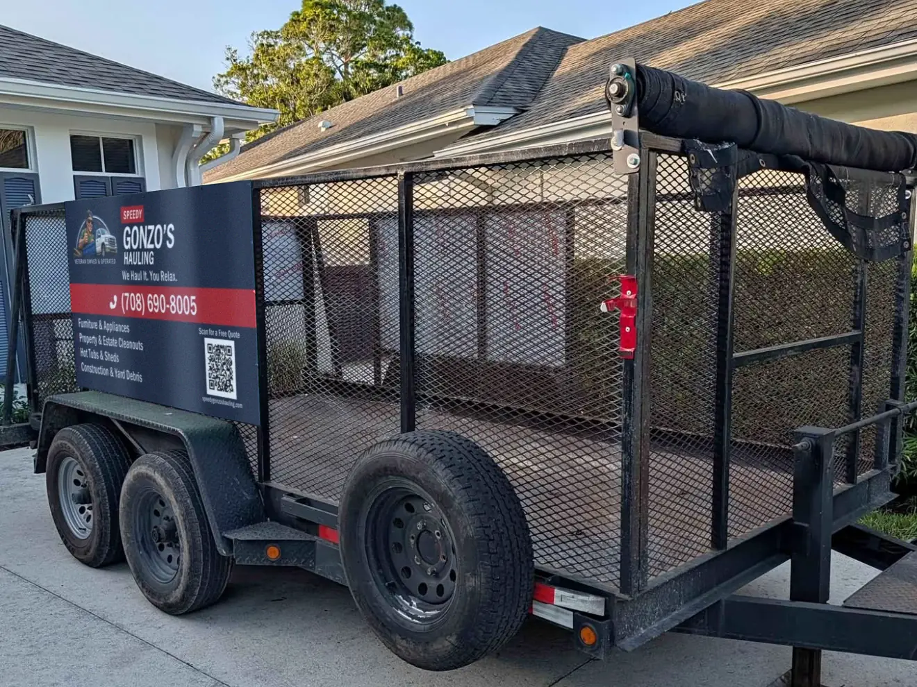 Speedy Gonzo's Hauling dump trailer parked on a concrete driveway - a black tandem-axle trailer with high mesh sides and the company's navy and red panel with the phone number on the front
