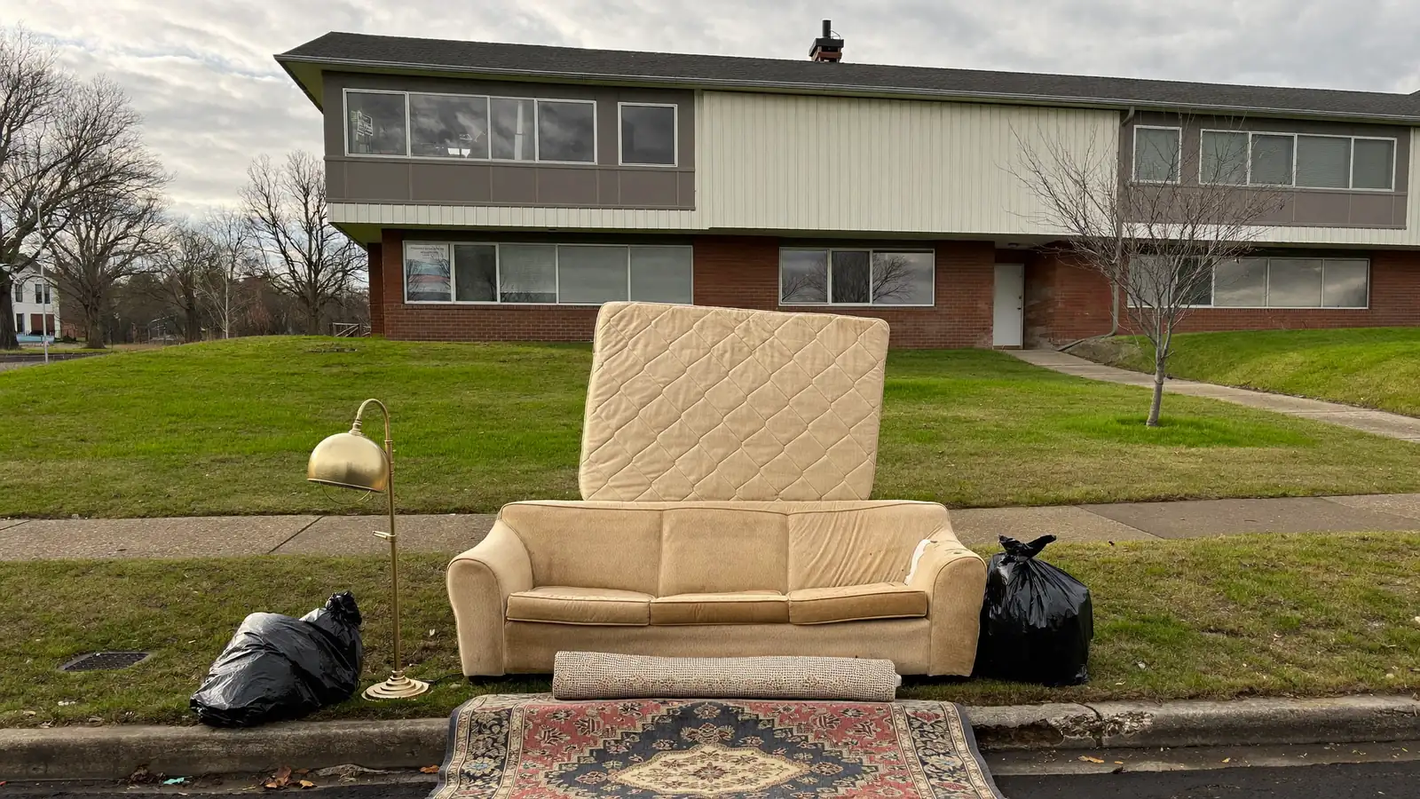 A couch, a mattress, and cardboard boxes set out at the curb in front of an apartment building